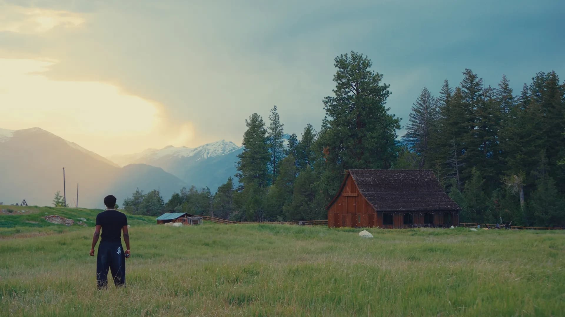 A creator in a Montana field at sunset, barn and mountains beyond